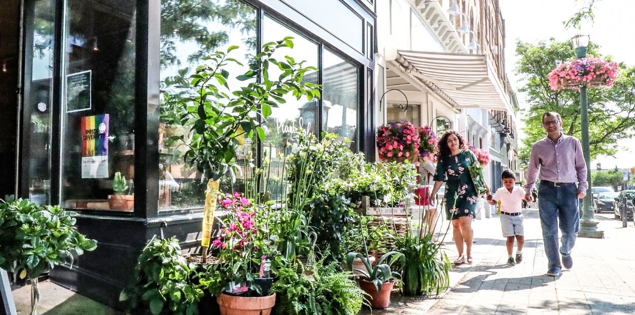 A family walking along a historic downtown street. They are near a florist with colourful flowers on display.